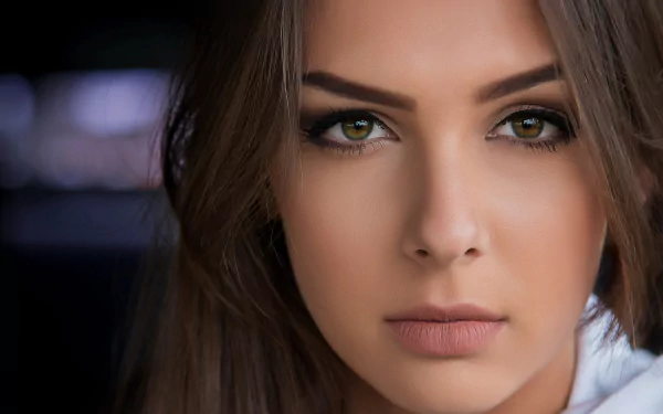 HD desktop wallpaper featuring a portrait of a model. The woman has striking green eyes, well-defined eyebrows, and long, brown hair, with an expressive and contemplative look on her face.