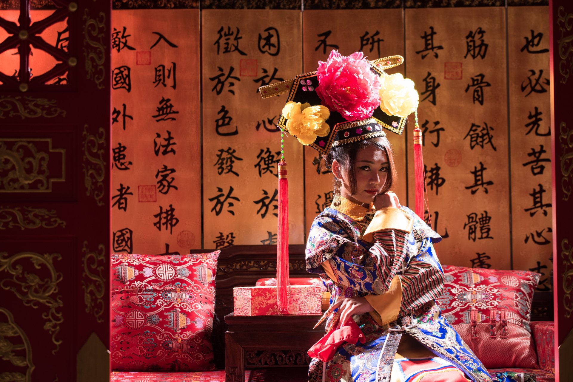 A woman dressed in traditional Taiwanese Chinese costume, Qián Fūrén style, poses gracefully on a sofa against a backdrop of calligraphy, captured in 4K Ultra HD.