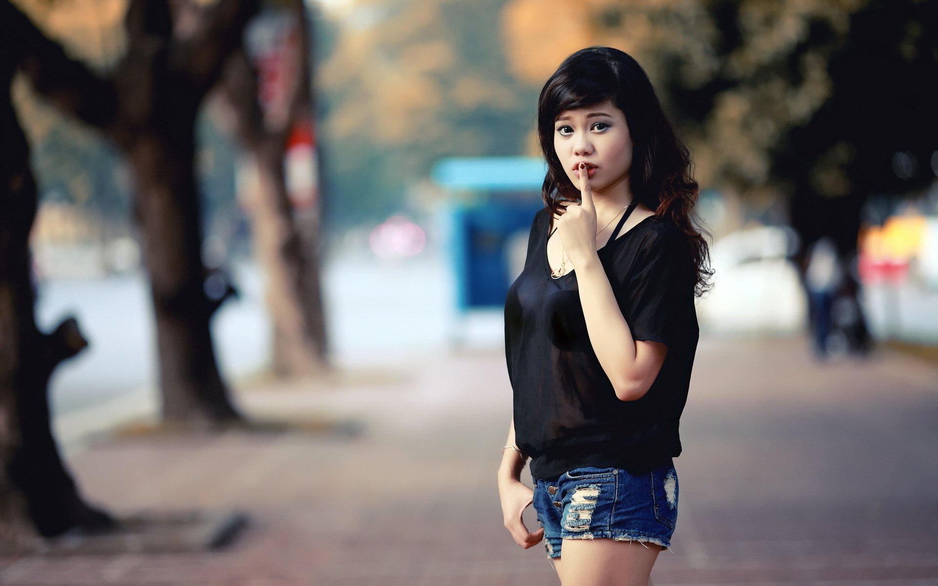 A beautiful woman stands on a blurred urban street, featured in a sharp HD PC desktop wallpaper and background.