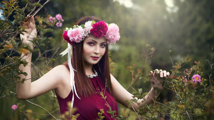 A beautiful woman with a floral crown poses among vibrant flowers, set against a serene, natural background, making it an enchanting HD desktop wallpaper.