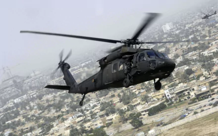 A Sikorsky UH-60 Black Hawk military helicopter in flight over an urban area, featured as an HD PC desktop wallpaper and background.