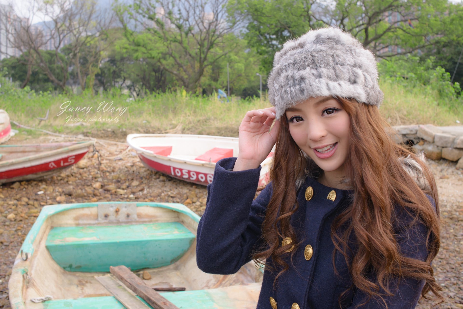 HD desktop wallpaper of a smiling Asian woman wearing a cap, posing by boats in a natural outdoor setting, featuring model Jancy Wong.