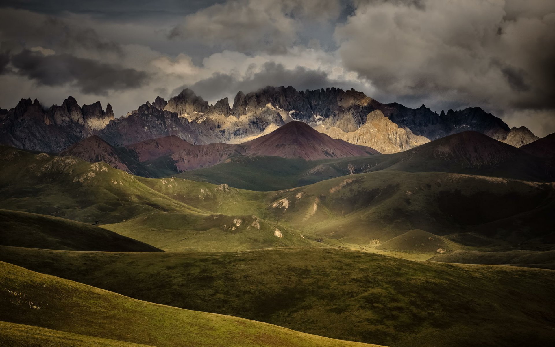 HD desktop wallpaper featuring the jagged peaks of the Bayan Har Mountains in Sichuan, China, under a dramatic sunset-lit sky.