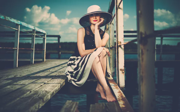 A vintage-style portrait of a woman in a wide-brimmed hat and striped skirt sitting barefoot on a wooden dock under a bright sky, 4K Ultra HD PC desktop wallpaper.