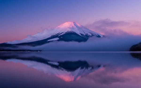 Mount Fuji rises majestically, shrouded in fog, its reflection shimmering in calm waters. Bathed in purple hues, this stunning natural scene captures Japan's serene beauty.