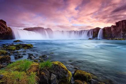 A stunning view of Goðafoss waterfall in Iceland, showcasing cascading water surrounded by lush greenery and a vibrant sky. This HD desktop wallpaper captures the beauty of nature.