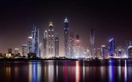A stunning night view of Dubai's skyline, featuring towering skyscrapers illuminated against the dark sky, with vibrant reflections shimmering in the water. A captivating cityscape backdrop.