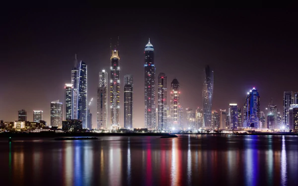 A stunning night view of Dubai's skyline, featuring towering skyscrapers illuminated against the dark sky, with vibrant reflections shimmering in the water. A captivating cityscape backdrop.