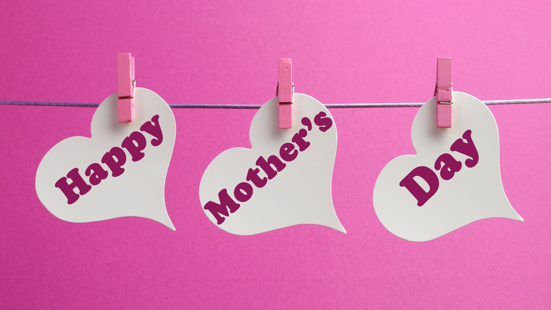 HD desktop wallpaper featuring three white heart-shaped notes clipped on a string with pink clothespins, each displaying the words Happy Mother's Day on a pink background.