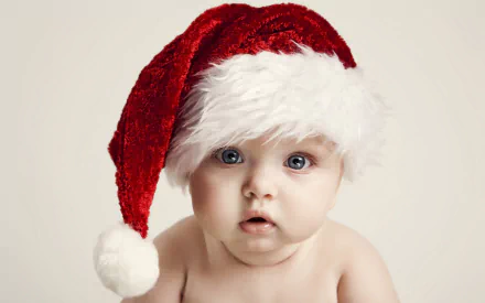 A cute baby wearing a fluffy Santa hat gazes curiously at the camera, capturing the festive spirit of Christmas in this charming HD photography background.