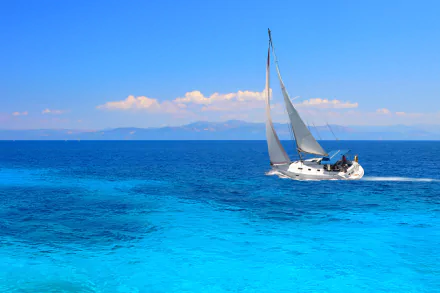 HD desktop wallpaper of a white sailboat gliding on vibrant blue ocean waters under a clear sky.