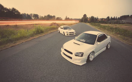 HD PC desktop wallpaper: two white Subaru WRX cars parked on a rural road at sunset, sporty vehicle shot.