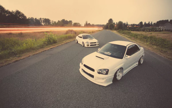 HD PC desktop wallpaper: two white Subaru WRX cars parked on a rural road at sunset, sporty vehicle shot.