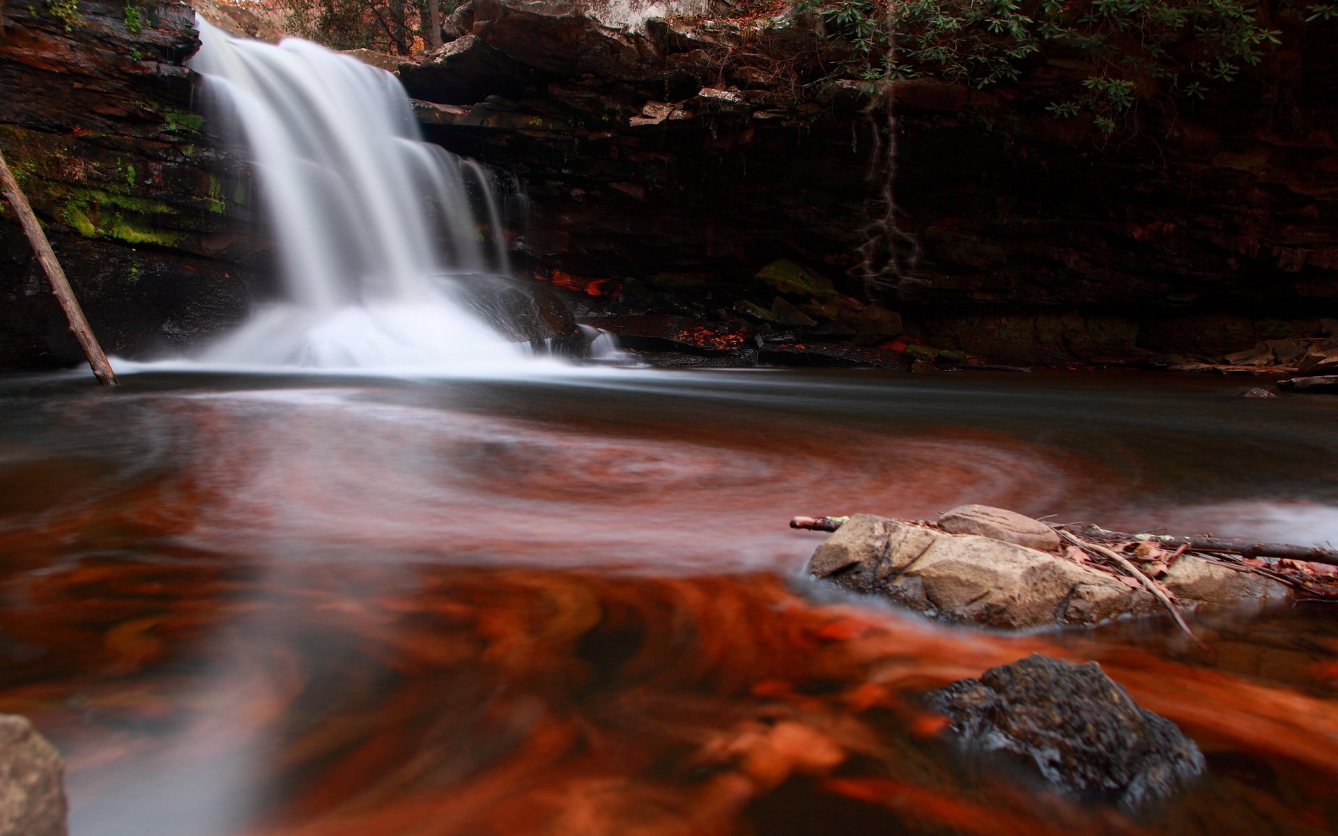 Mill Creek Waterfall in West Virginia flowing into a calm pond framed by red-brown rocks and forest; silky long-exposure water, 2K Quad HD PC desktop wallpaper background.