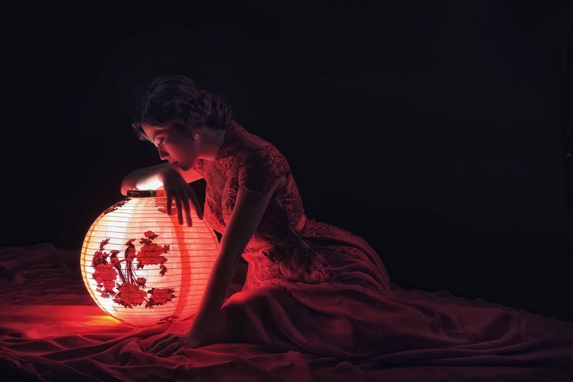 Asian woman in traditional attire leans on a glowing ornamental lantern, set against a dark background, creating a serene and elegant HD desktop wallpaper.