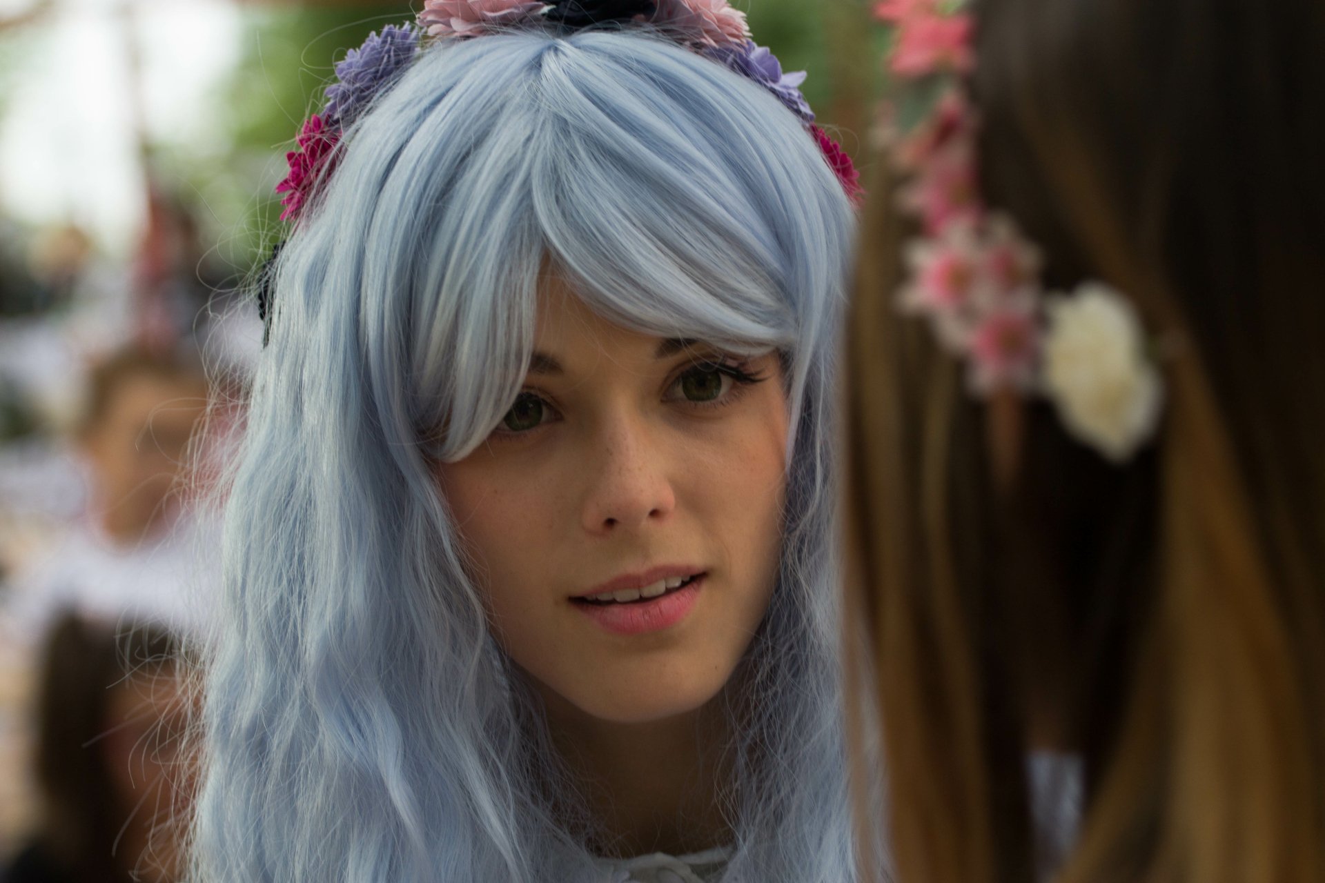 A woman with blue hair and floral accessories engages intensely, captured in bokeh, showcasing her captivating expression in this 4K Ultra HD wallpaper.