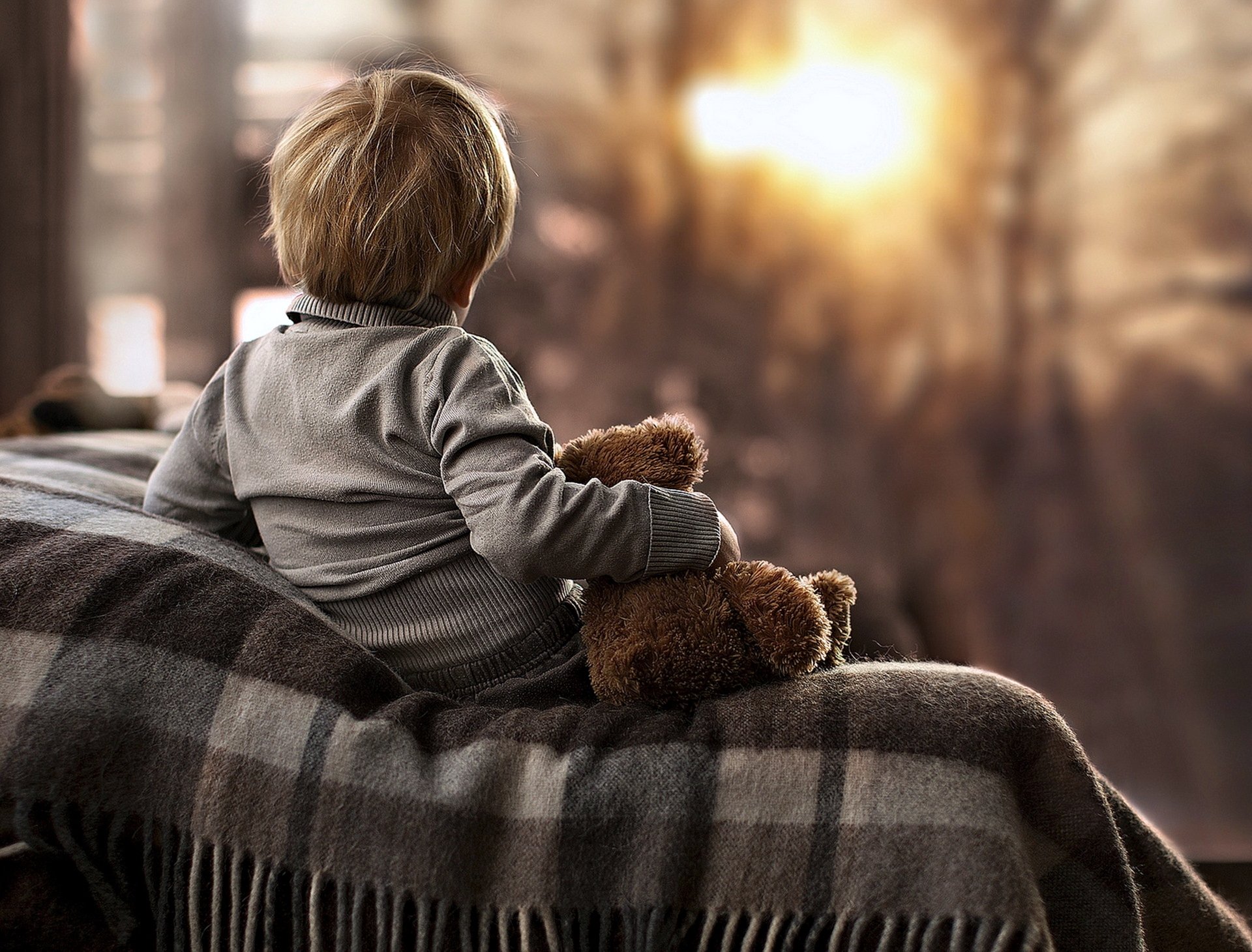 A child gently holding a teddy bear, sitting on a blanket with warm sunlight filtering through, captured in 4K Ultra HD photography for a PC desktop wallpaper.