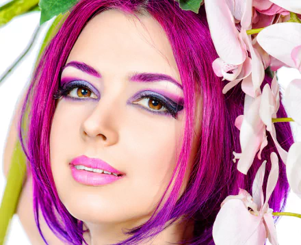 A woman with striking crimson hair and vibrant makeup gazes at the viewer, framed by delicate flowers, creating a captivating HD wallpaper and background.