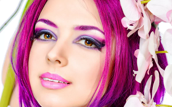 A woman with striking crimson hair and vibrant makeup gazes at the viewer, framed by delicate flowers, creating a captivating HD wallpaper and background.