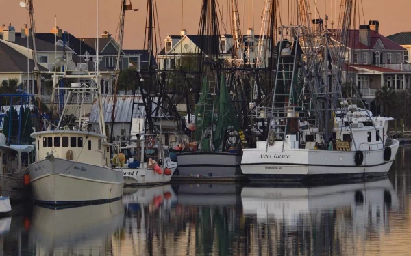 A tranquil harbor scene showcases fishing boats docked alongside charming waterfront homes, reflecting beautifully on still waters, creating a captivating HD desktop wallpaper.