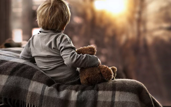 A child gently holding a teddy bear, sitting on a blanket with warm sunlight filtering through, captured in 4K Ultra HD photography for a PC desktop wallpaper.