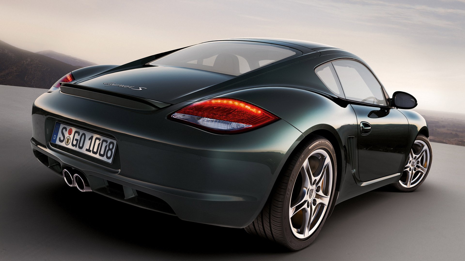 HD desktop wallpaper featuring a sleek green Porsche Cayman S car, highlighting its sporty design and elegant curves on a smooth road background.