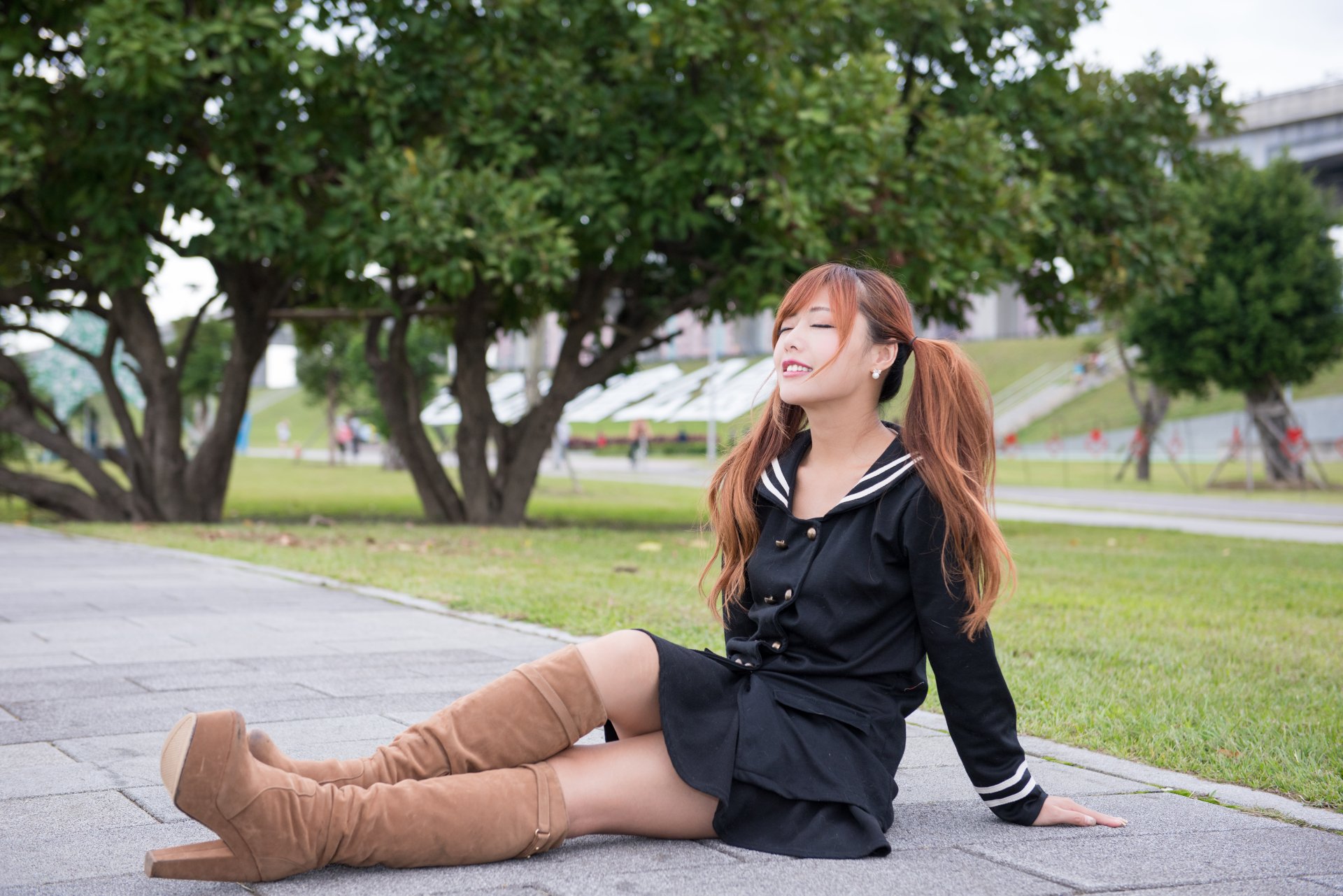 A Taiwanese Asian woman model, Xiao Xi, wearing boots and a black outfit, sits on a paved path near green trees in this 4K Ultra HD PC desktop wallpaper.