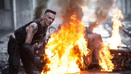 Ninja (Watkin Tudor Jones) from the movie Chappie crouches near a large fire in this 4K Ultra HD PC desktop wallpaper and background.