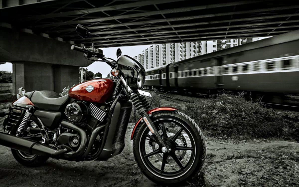 A striking Harley-Davidson motorcycle stands under a bridge, with a train passing in the background, captured in a dramatic black-and-white style for a captivating HD wallpaper.