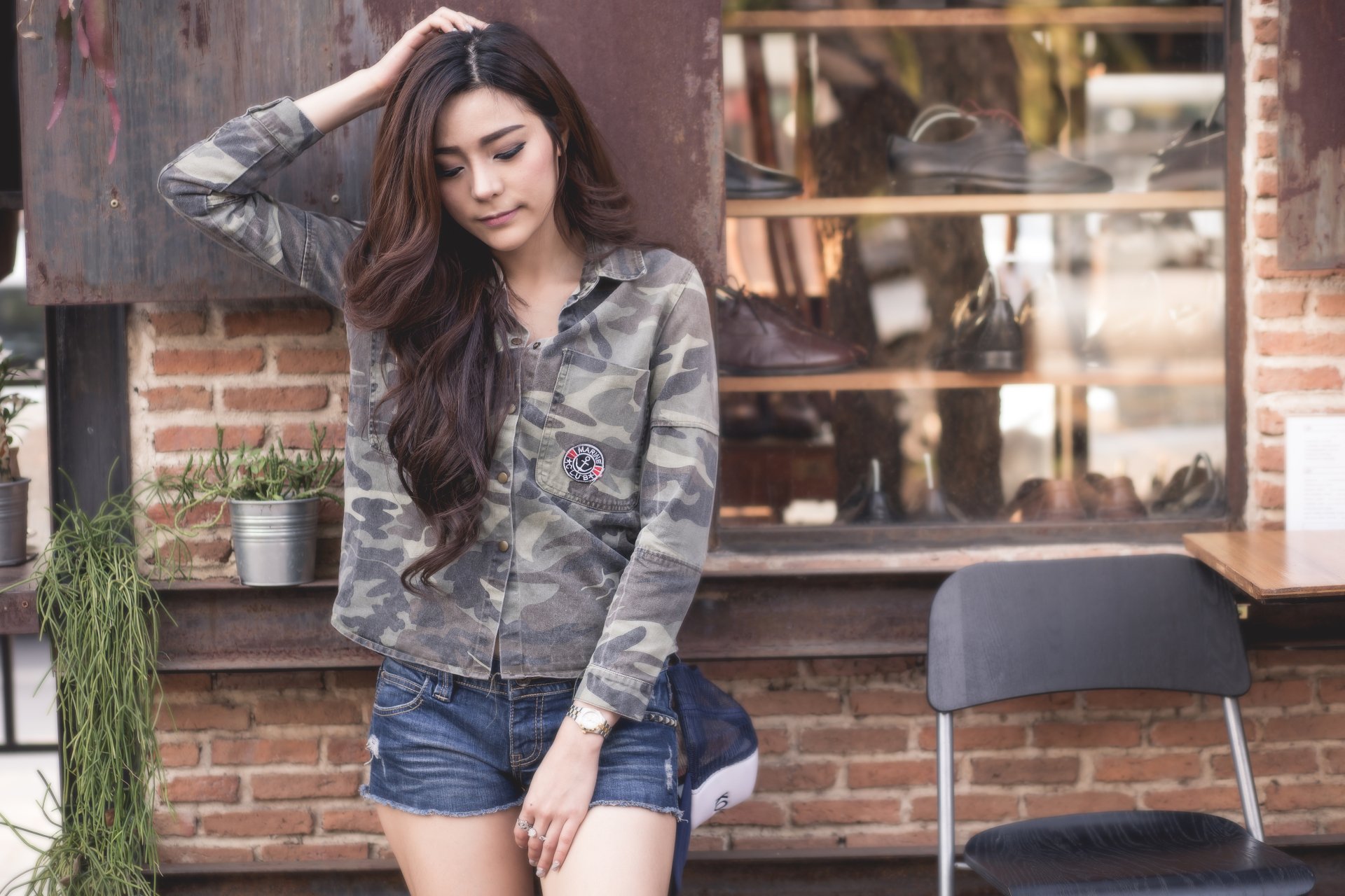 A woman with long, dark hair models a khaki camo jacket and denim shorts in front of a brick wall, tagged Kookai. The image, featuring an Asian model, is an HD desktop wallpaper and background.