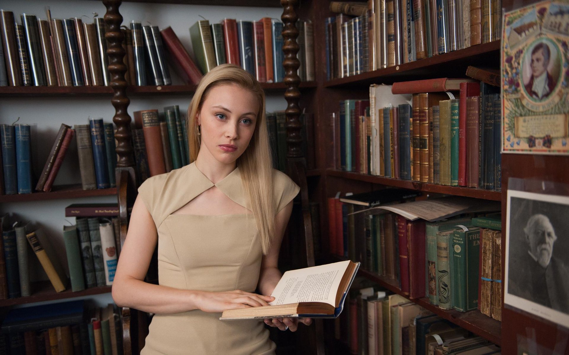 Canadian actress Sarah Gadon with blue eyes and blonde hair reads a book in a vintage library setting, inspired by the movie Cosmopolis.