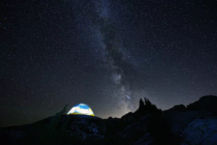 A glowing tent sits under a stunning starry sky, featuring the Milky Way, capturing the beauty of camping at night in this HD desktop wallpaper.