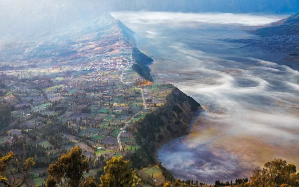 A breathtaking view of a fog-covered village nestled in a valley in Java, Indonesia, showcasing the serene landscape captured in stunning HD photography.