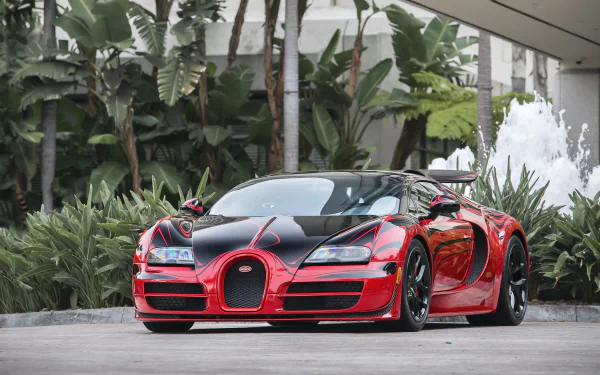 A striking Bugatti Veyron showcased in vibrant red and black, surrounded by lush greenery, serves as an impressive HD desktop wallpaper for car enthusiasts and tuning aficionados.