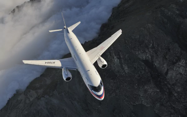 4K Ultra HD image of a Sukhoi SuperJet 100 jet airplane flying over mountainous terrain, showcasing its sleek design and modern aviation technology.