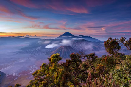 HD desktop wallpaper of Mount Bromo in Java, Indonesia, captures a breathtaking sunrise over the stratovolcano surrounded by lush greenery and a beautiful, colorful sky.