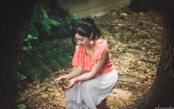 A Taiwanese model, Chén Sīyǐng, sits amidst fallen leaves in a serene outdoor setting, wearing a soft pink top and white skirt, capturing the essence of autumn.