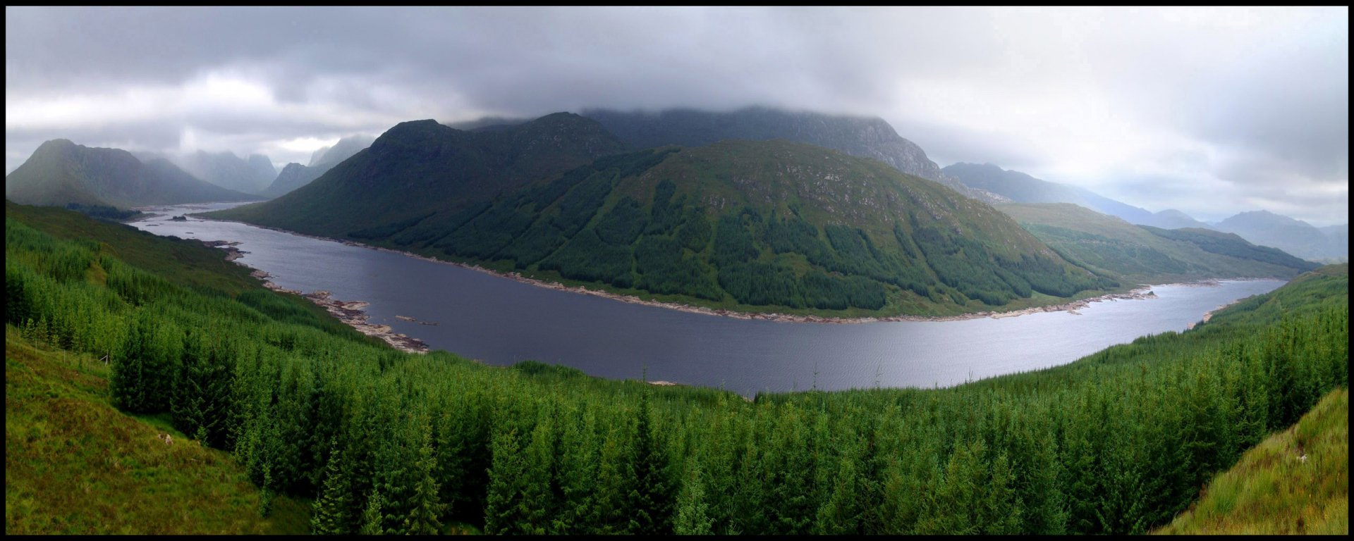 HD desktop wallpaper showcasing a serene river winding through lush green forests with mist-covered mountains under a cloudy sky in a nature landscape.