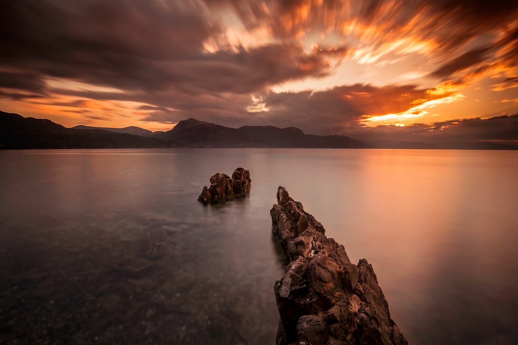 HD PC desktop wallpaper and background: nature scene of jagged rock outcrops stretching into calm sea at sunset beneath dramatic clouds.