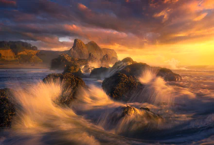 HD PC desktop wallpaper: dramatic coastline at sunset, rocky shore with crashing ocean waves and golden light sweeping across the surf.
