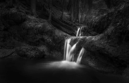 Black and white HD desktop wallpaper of a serene waterfall cascading into a stream surrounded by natural rock formations.