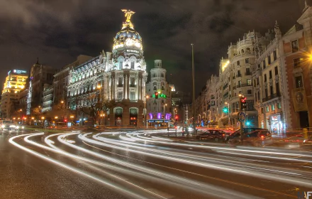 A vibrant nighttime cityscape of Madrid with illuminated historic buildings and dynamic light trails from traffic, captured in 4K Ultra HD for a PC desktop wallpaper.