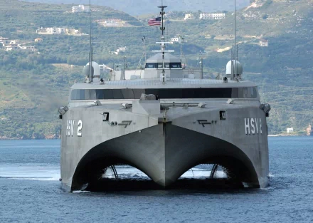 Front view of the military warship, HSV-2 Swift, on calm water with land in the background. The image is a high-definition desktop wallpaper featuring the navy ship.