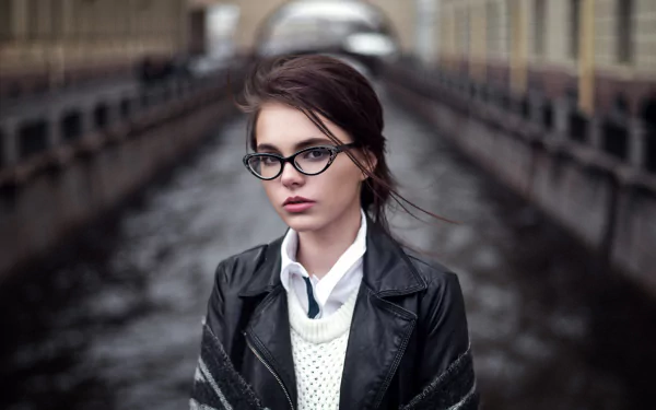 HD desktop wallpaper of a brunette woman with brown eyes wearing glasses and a leather jacket, set against a blurred bokeh background, photographed by Oktyabrina Maximova.