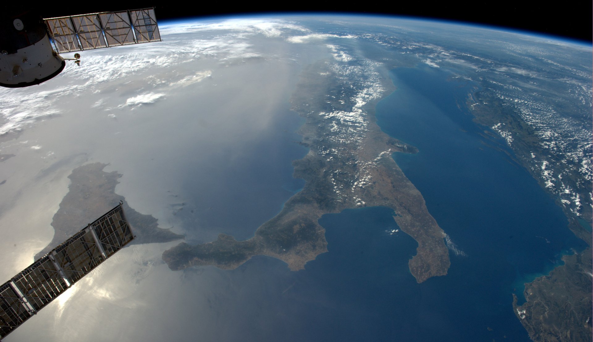 4K Ultra HD desktop wallpaper: orbital station solar panels frame a cloud-swept Mediterranean, Sicily and the Apennine boot of Italy seen from Earth orbit.