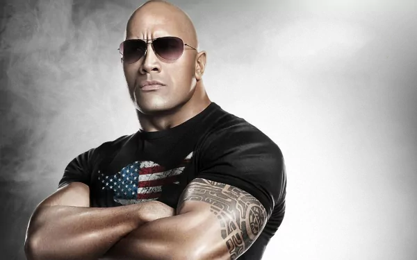 HD desktop wallpaper featuring bald American actor Dwayne Johnson wearing sunglasses and a tattooed arm, dressed in a black shirt with an American flag design.