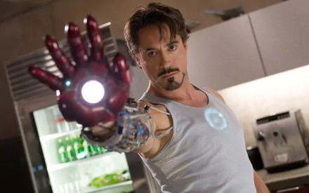 HD desktop wallpaper featuring Robert Downey Jr. as Tony Stark in the movie Iron Man, with Stark in his workshop, wearing the Iron Man armor and extending his hand with a glowing repulsor.