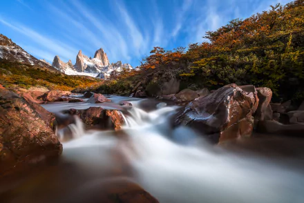 HD desktop wallpaper of a serene mountain landscape in Argentina, featuring a flowing river and colorful autumn foliage under a vibrant blue sky.