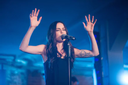 Lena Meyer-Landrut performs passionately on stage, microphone in hand, in a vibrant blue-lit setting. This HD image serves as a striking music-themed desktop wallpaper.