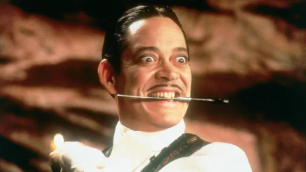Gomez Addams from Addams Family Values grins mischievously, holding a candle while balancing a cigarette holder in his mouth, showcasing the quirky charm of the iconic character.